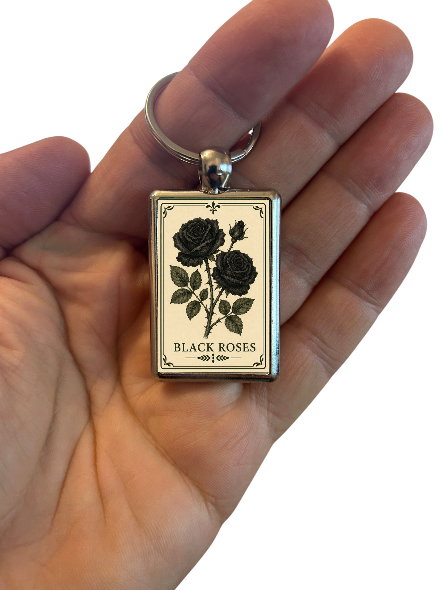 Keychain with black roses design held in a hand against a white background