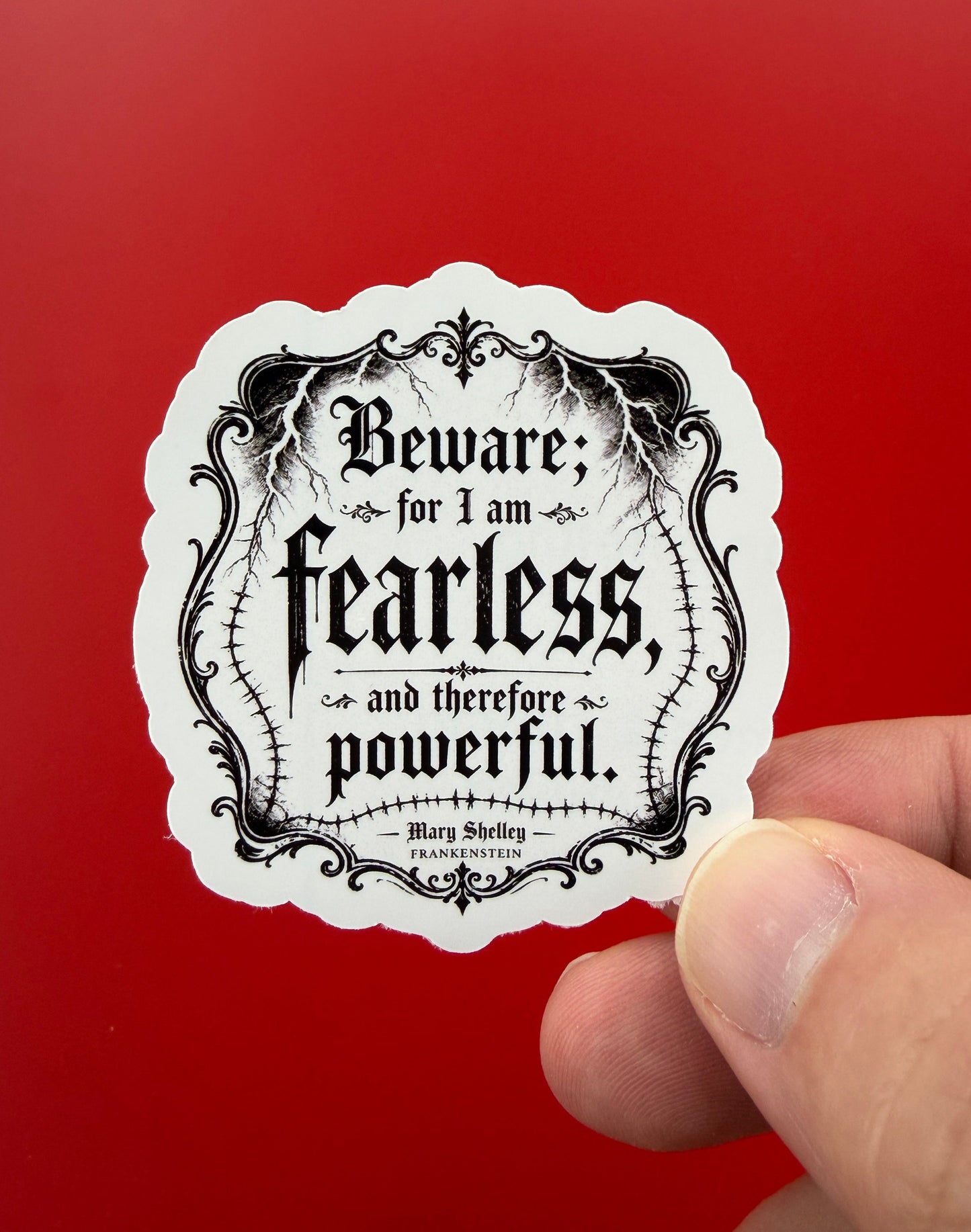 Hand holding a black and white sticker with text against a red background